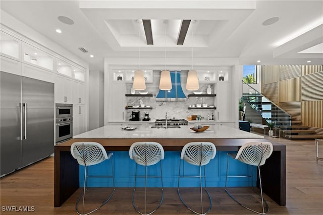 kitchen with custom range hood, dark wood-style flooring, backsplash, white cabinets, and appliances with stainless steel finishes