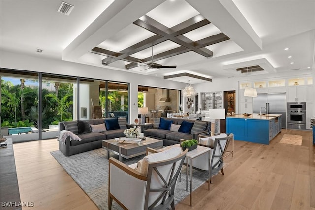 living area featuring coffered ceiling, beamed ceiling, ceiling fan with notable chandelier, visible vents, and light wood-style floors