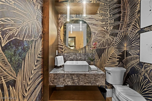 bathroom featuring a sink, toilet, and wallpapered walls
