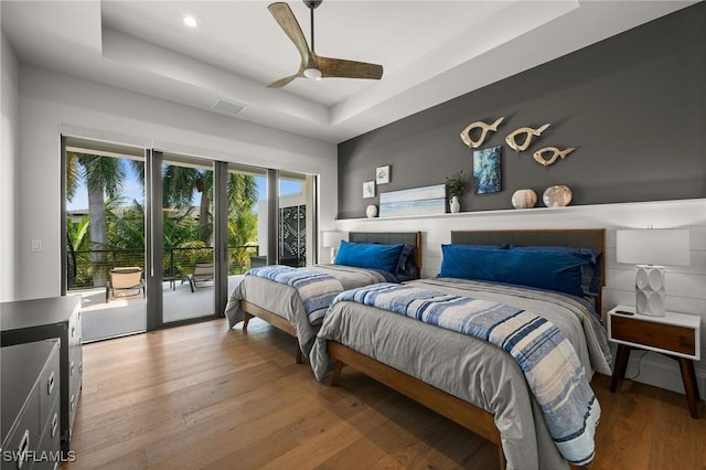 bedroom featuring a raised ceiling, light wood-style floors, and access to exterior