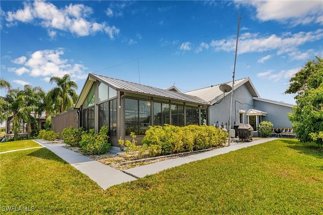 view of home's exterior with a lawn, metal roof, and a sunroom