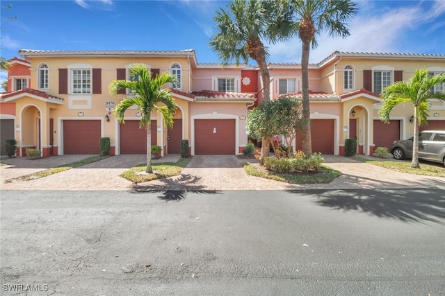 mediterranean / spanish house with a garage, stucco siding, driveway, and a tile roof