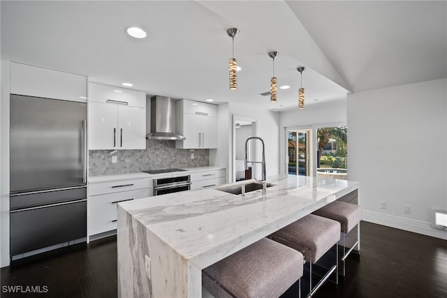 kitchen with wall chimney range hood, a sink, modern cabinets, stainless steel appliances, and white cabinetry
