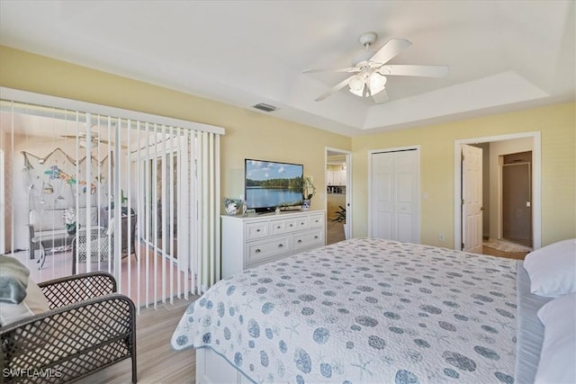 bedroom with a ceiling fan, visible vents, a raised ceiling, light wood-style floors, and access to outside