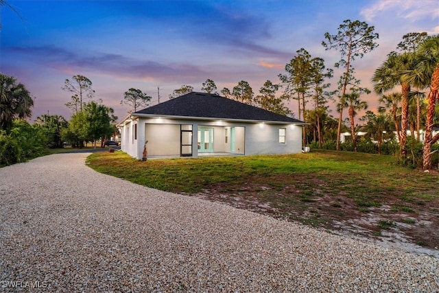 2312 4th Ave SE, Naples, FL 34117 - back of house at dusk with a yard, stucco siding, a shingled roof, and gravel driveway
