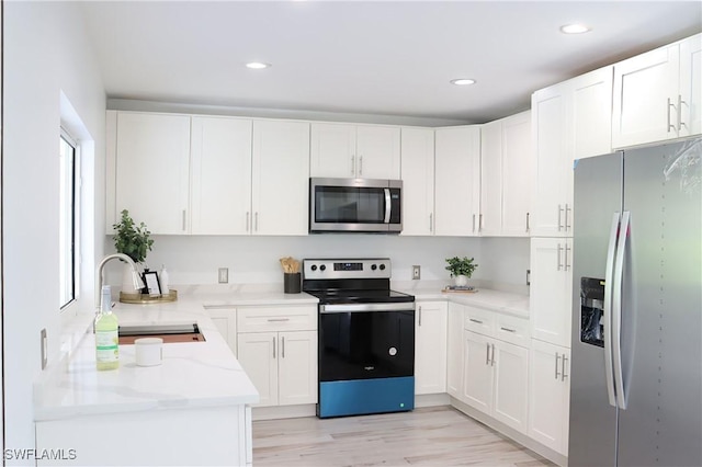 kitchen with light wood finished floors, light stone countertops, stainless steel appliances, white cabinetry, and a sink
