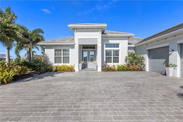 view of front of property featuring decorative driveway, french doors, an attached garage, and stucco siding