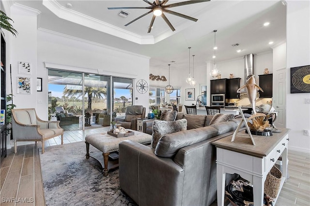 living room with wood finish floors, visible vents, a ceiling fan, and ornamental molding