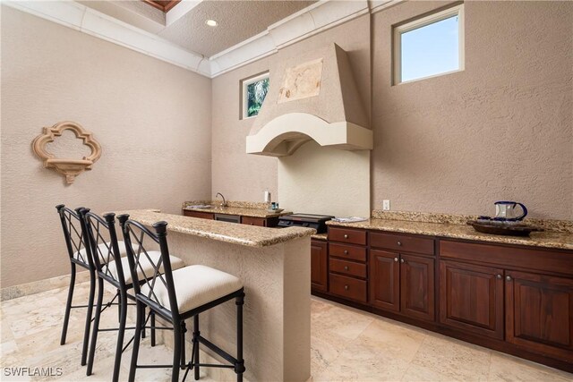 23771 Tuscany Way, Bonita Springs, FL 34134 - kitchen with a breakfast bar area, recessed lighting, a textured wall, ornamental molding, and light stone counters