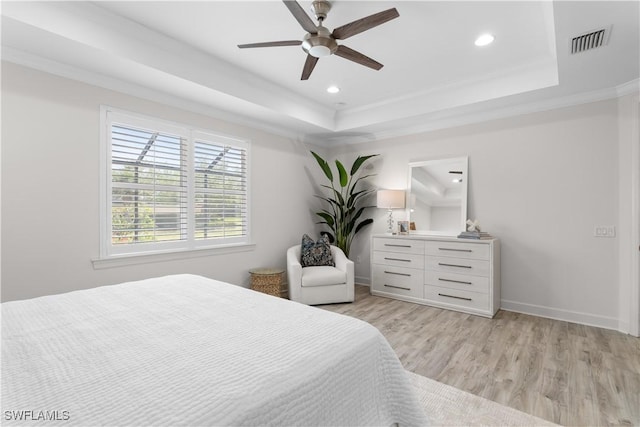 bedroom with a tray ceiling, light wood-type flooring, baseboards, and visible vents