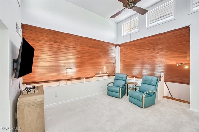 sitting room featuring a towering ceiling, carpet, wood walls, baseboards, and ceiling fan