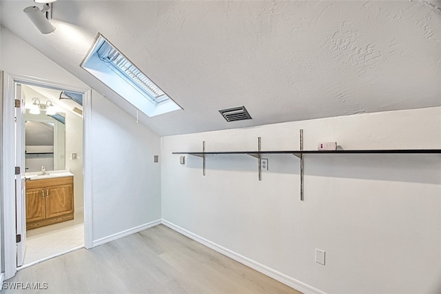 bonus room with visible vents, lofted ceiling with skylight, a textured ceiling, light wood-style floors, and baseboards