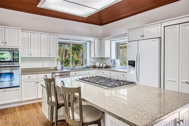 kitchen featuring light stone countertops, a sink, white cabinets, appliances with stainless steel finishes, and a center island