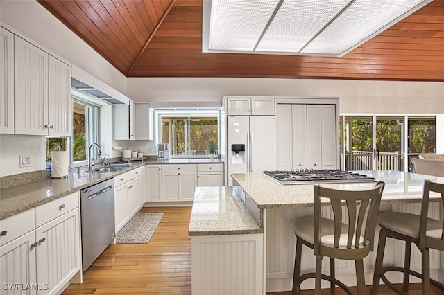 kitchen featuring light wood finished floors, a sink, vaulted ceiling, appliances with stainless steel finishes, and a center island