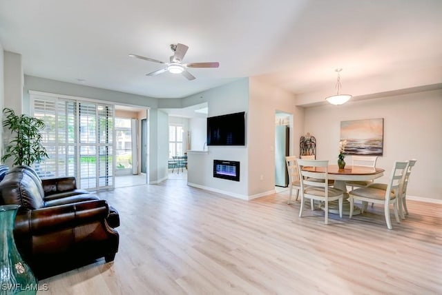 living area featuring a glass covered fireplace, ceiling fan, light wood-type flooring, and baseboards
