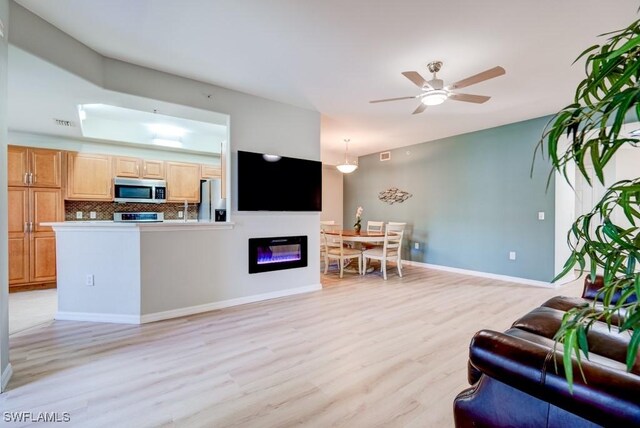 living area with light wood finished floors, a ceiling fan, visible vents, and a glass covered fireplace