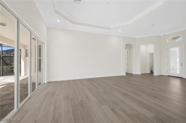 16404 Coco Hammock Way, Fort Myers, FL 33908 - unfurnished living room with arched walkways, ornamental molding, plenty of natural light, a tray ceiling, and light wood-style floors