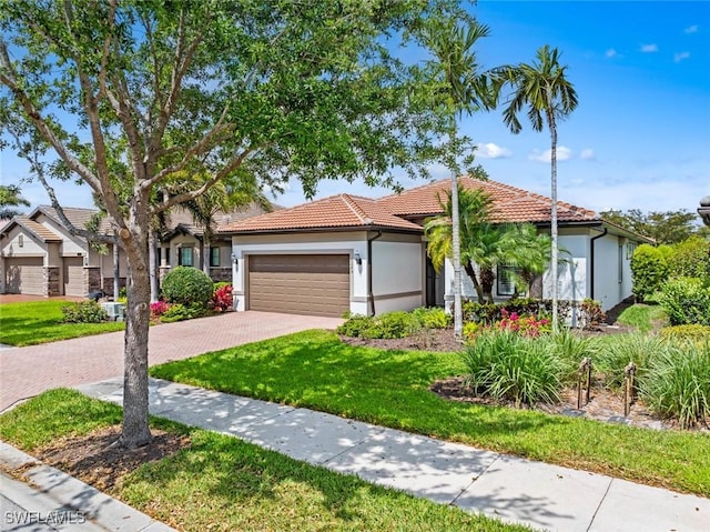 view of front facade featuring a front yard, an attached garage, stucco siding, a tiled roof, and decorative driveway
