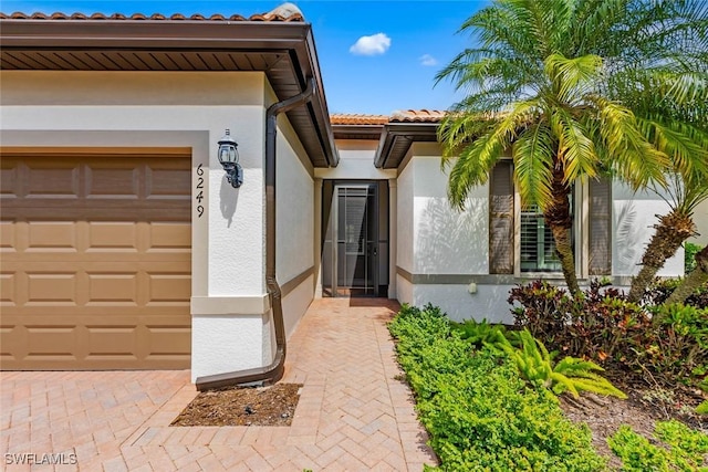 doorway to property with decorative driveway, a tiled roof, an attached garage, and stucco siding