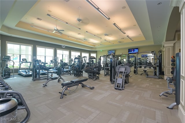 gym with light carpet, a ceiling fan, and a tray ceiling
