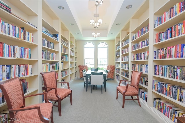 living area with visible vents, a tray ceiling, an inviting chandelier, carpet flooring, and wall of books