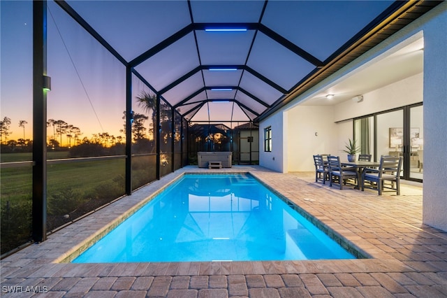 pool at dusk with glass enclosure, a patio, an outdoor pool, and a hot tub