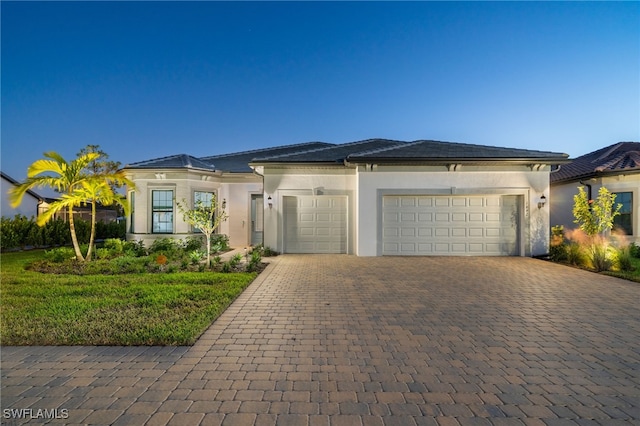 prairie-style house with stucco siding, decorative driveway, and an attached garage