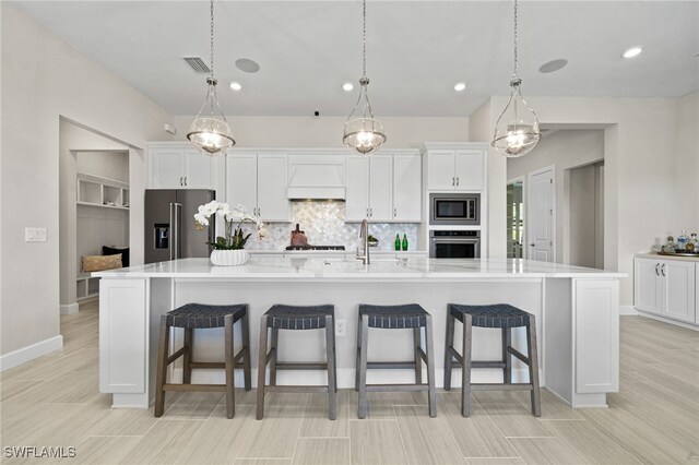 kitchen with visible vents, a kitchen bar, custom range hood, white cabinetry, and appliances with stainless steel finishes