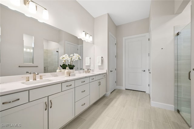 full bathroom featuring double vanity, a stall shower, baseboards, and a sink