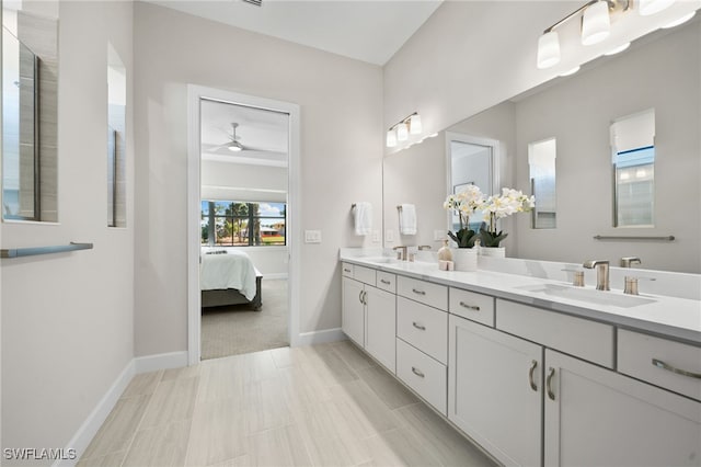 ensuite bathroom featuring a ceiling fan, baseboards, double vanity, a sink, and connected bathroom