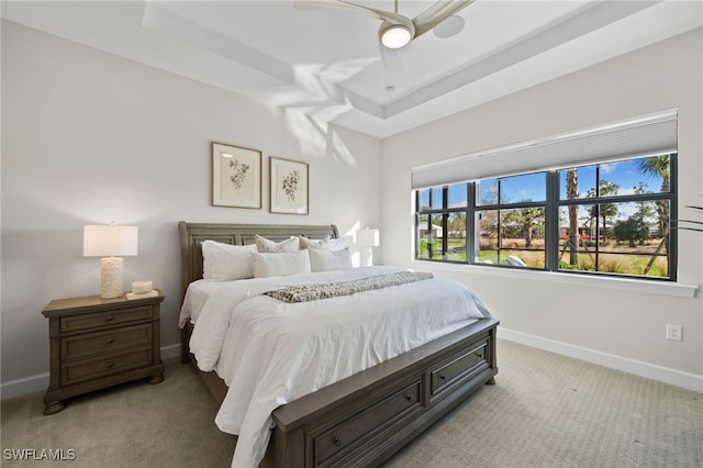 carpeted bedroom with baseboards, a raised ceiling, and a ceiling fan