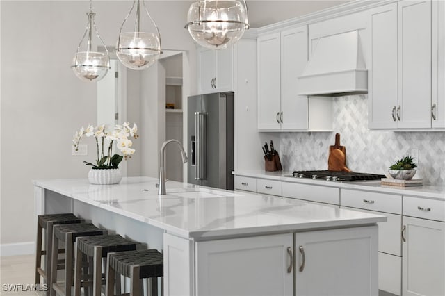 kitchen with tasteful backsplash, premium range hood, a center island with sink, appliances with stainless steel finishes, and white cabinets
