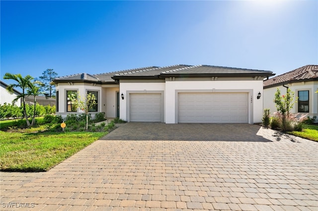 prairie-style house featuring a tile roof, decorative driveway, a garage, and stucco siding