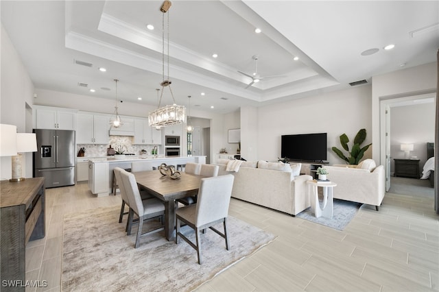dining space with visible vents, ceiling fan, wood finish floors, a tray ceiling, and ornamental molding