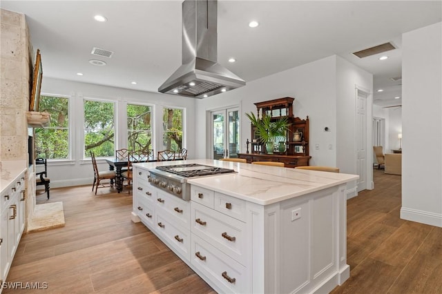 20732 Charing Cross Cir, Estero, FL 33928 - kitchen featuring island exhaust hood, stainless steel gas stovetop, white cabinetry, light wood finished floors, and light stone counters