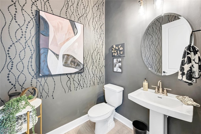 bathroom with baseboards, wood finished floors, toilet, and a sink