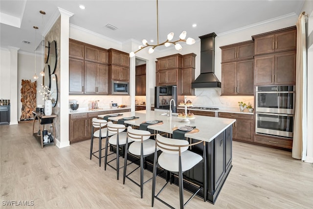 15445 Turin Dr, Naples, FL 34114 - kitchen featuring wall chimney exhaust hood, appliances with stainless steel finishes, light wood-style floors, a center island with sink, and light countertops