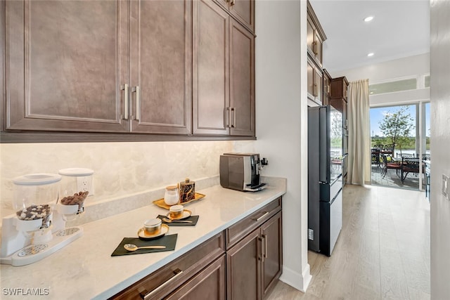 kitchen featuring freestanding refrigerator, light countertops, dark brown cabinetry, light wood-type flooring, and recessed lighting