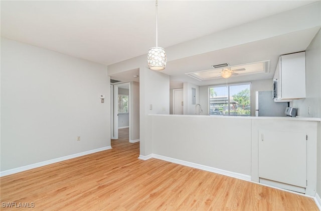 kitchen featuring baseboards, freestanding refrigerator, white cabinets, decorative light fixtures, and light wood-type flooring