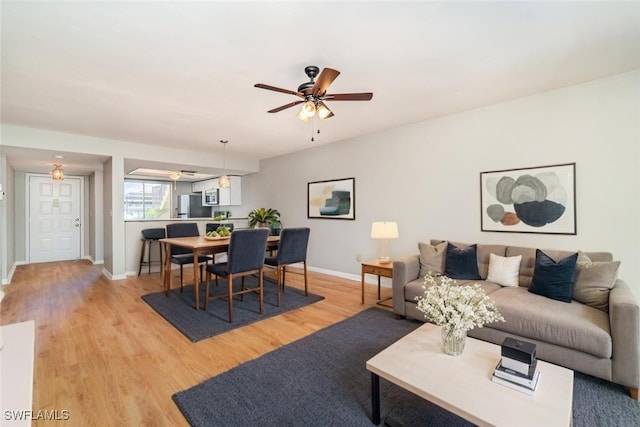 living room featuring baseboards, light wood-type flooring, and a ceiling fan