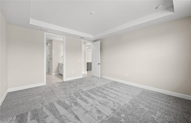 unfurnished bedroom featuring carpet floors, a raised ceiling, ensuite bathroom, and baseboards