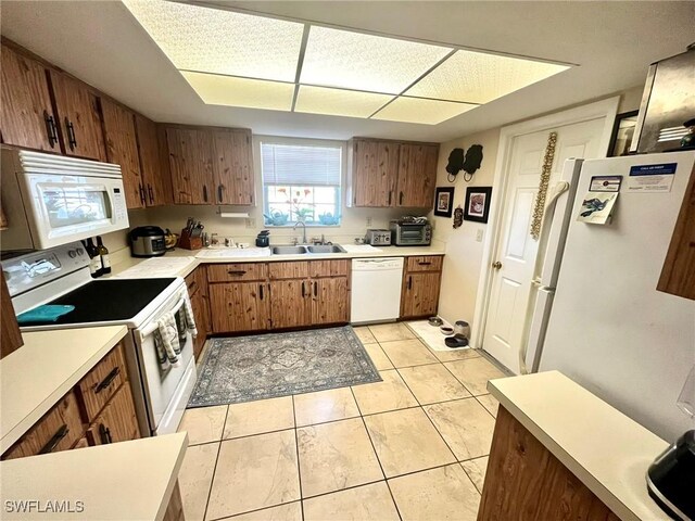 kitchen featuring light countertops, light tile patterned floors, brown cabinetry, white appliances, and a sink