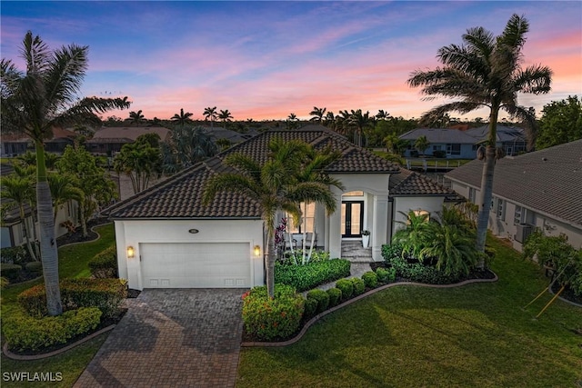 mediterranean / spanish house featuring stucco siding, a garage, a tiled roof, decorative driveway, and a lawn