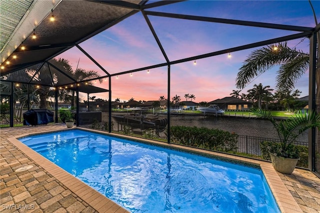 pool at dusk featuring an outdoor pool, a patio, a grill, and a lanai