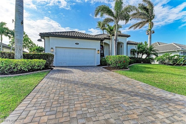 mediterranean / spanish-style home featuring stucco siding, a tile roof, decorative driveway, a front yard, and an attached garage