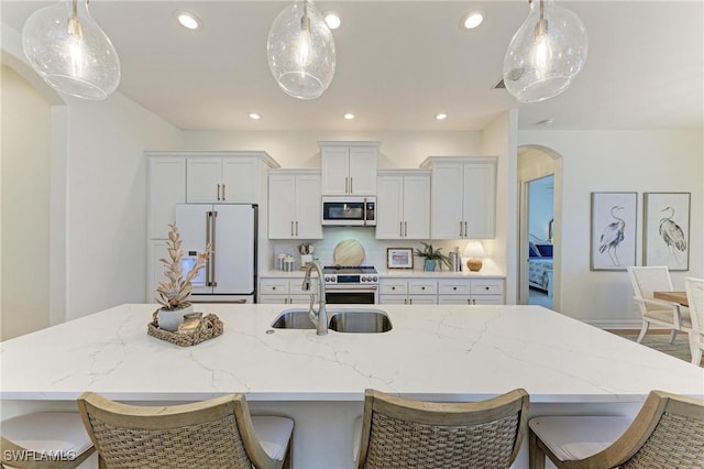 kitchen featuring a spacious island, premium appliances, recessed lighting, arched walkways, and a sink