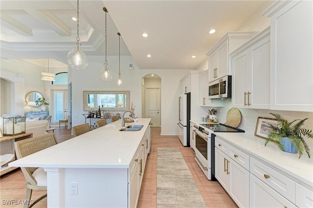 kitchen with white appliances, a breakfast bar area, a kitchen island with sink, arched walkways, and white cabinets