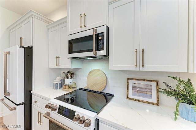 kitchen with tasteful backsplash, stove, white cabinets, and freestanding refrigerator