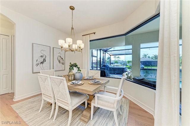 dining space with arched walkways, an inviting chandelier, baseboards, and light wood-style floors