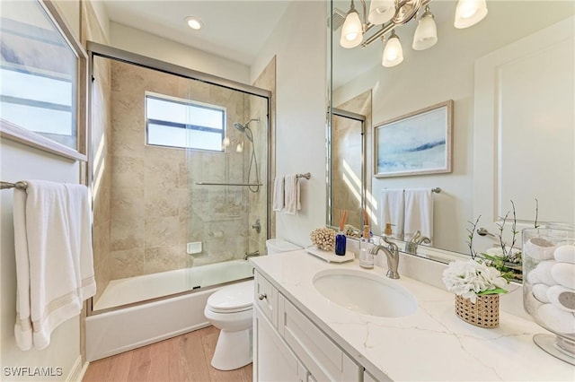full bathroom featuring toilet, wood finished floors, an inviting chandelier, enclosed tub / shower combo, and vanity